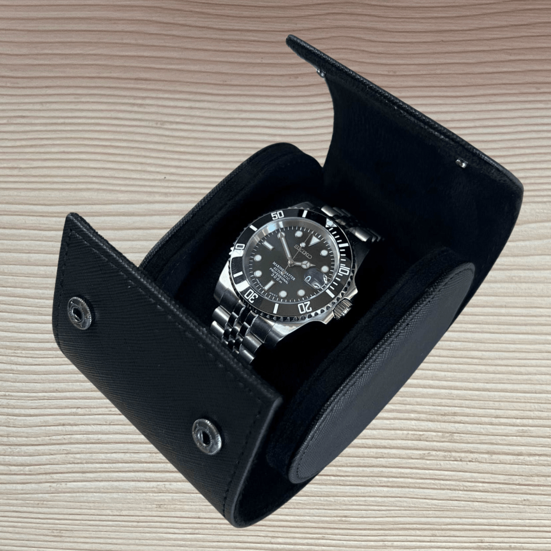 Étui de voyage noir ModTime pour une montre, montre présentée sur un coussin à l'intérieur, vue ouverte en biais sur du bois