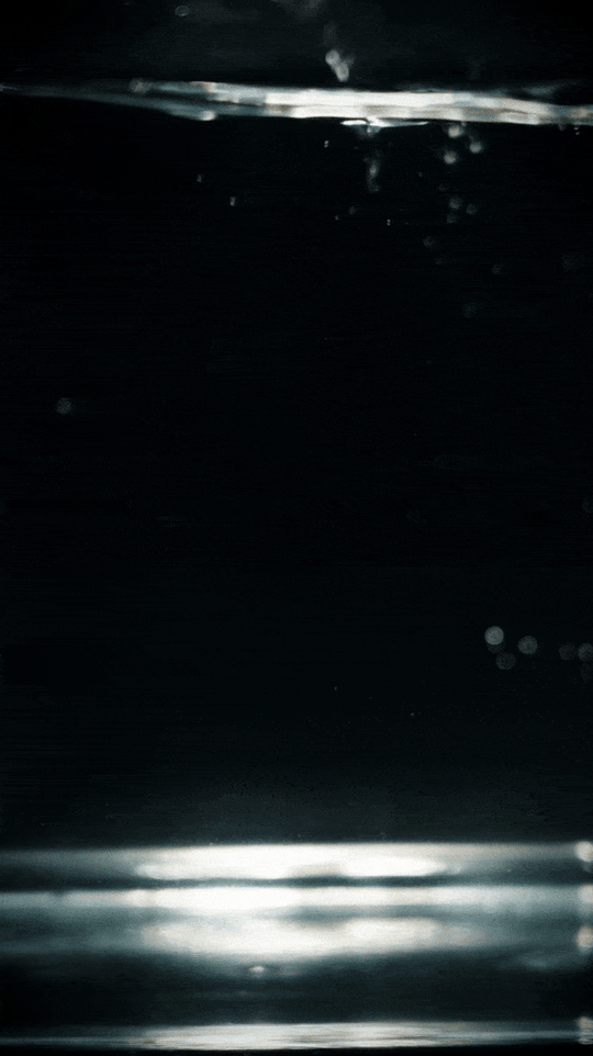 Black-dial chronograph with a silver-tone bracelet moving through water, surrounded by bubbles