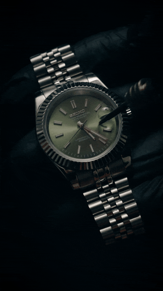 Soft brush cleaning the crystal of a green-dial Datejust-style watch held in a gloved hand