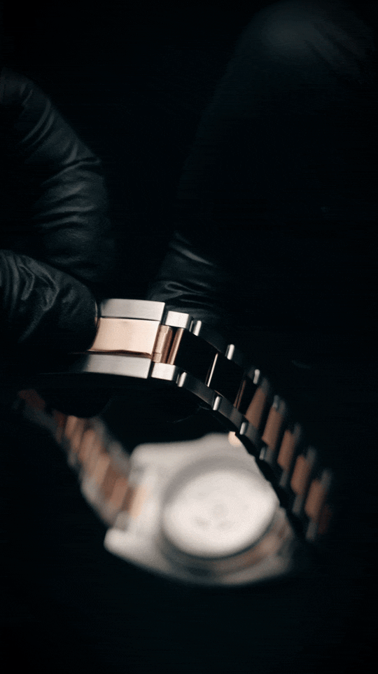 Gloved hands holding a two-tone silver and rose-tone watch bracelet, animated close-up of the links