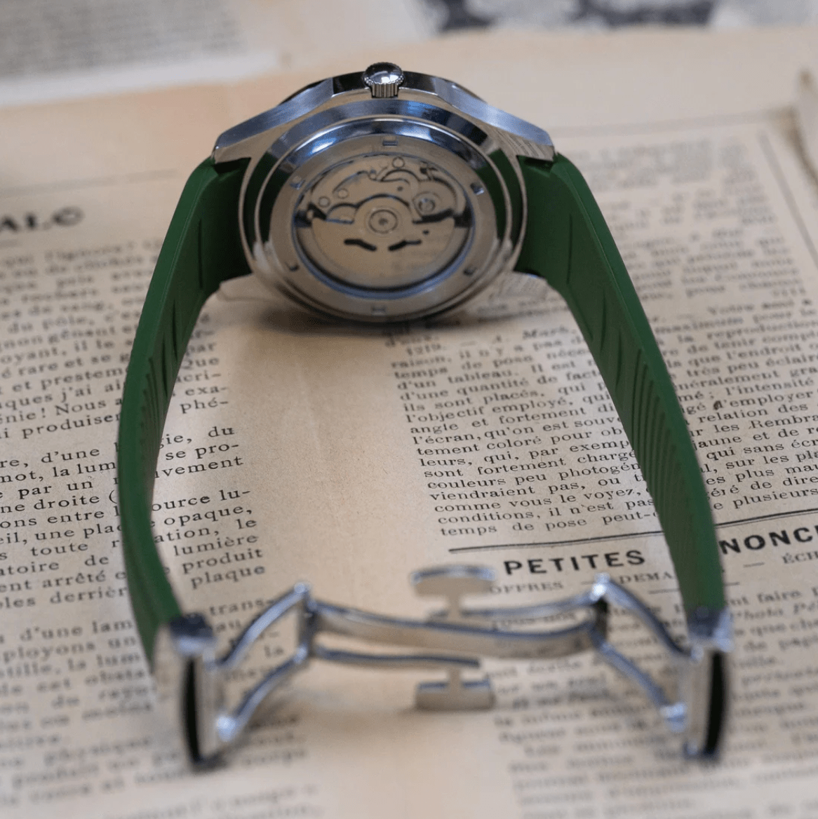 Montre automatique ModTime de style Aquanaut — configuration verte (NH35), bracelet vert, fond de boîtier transparent, vue arrière sur un journal
