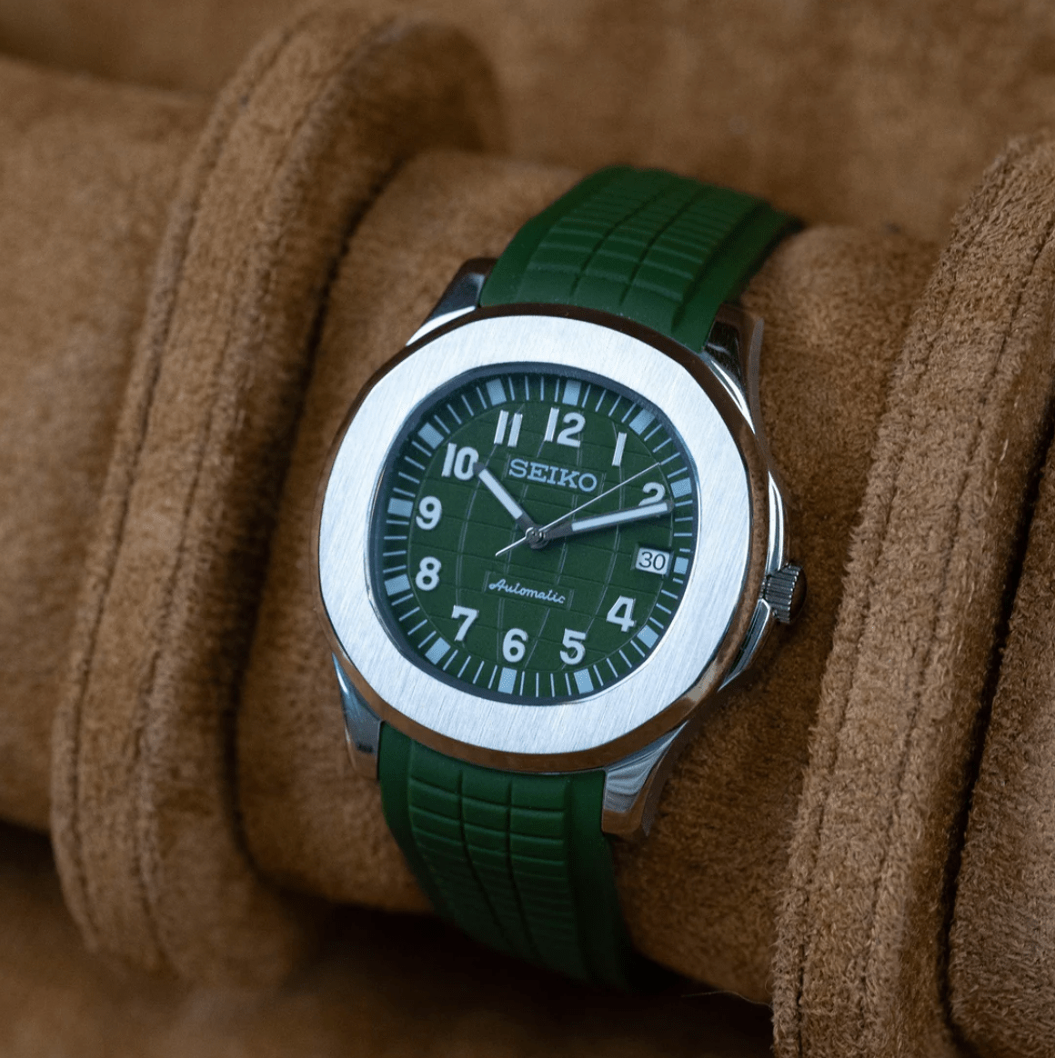 Montre automatique ModTime de style Aquanaut — configuration verte (NH35), bracelet vert, lunette brossée, vue en biais côté droit sur un coussin marron