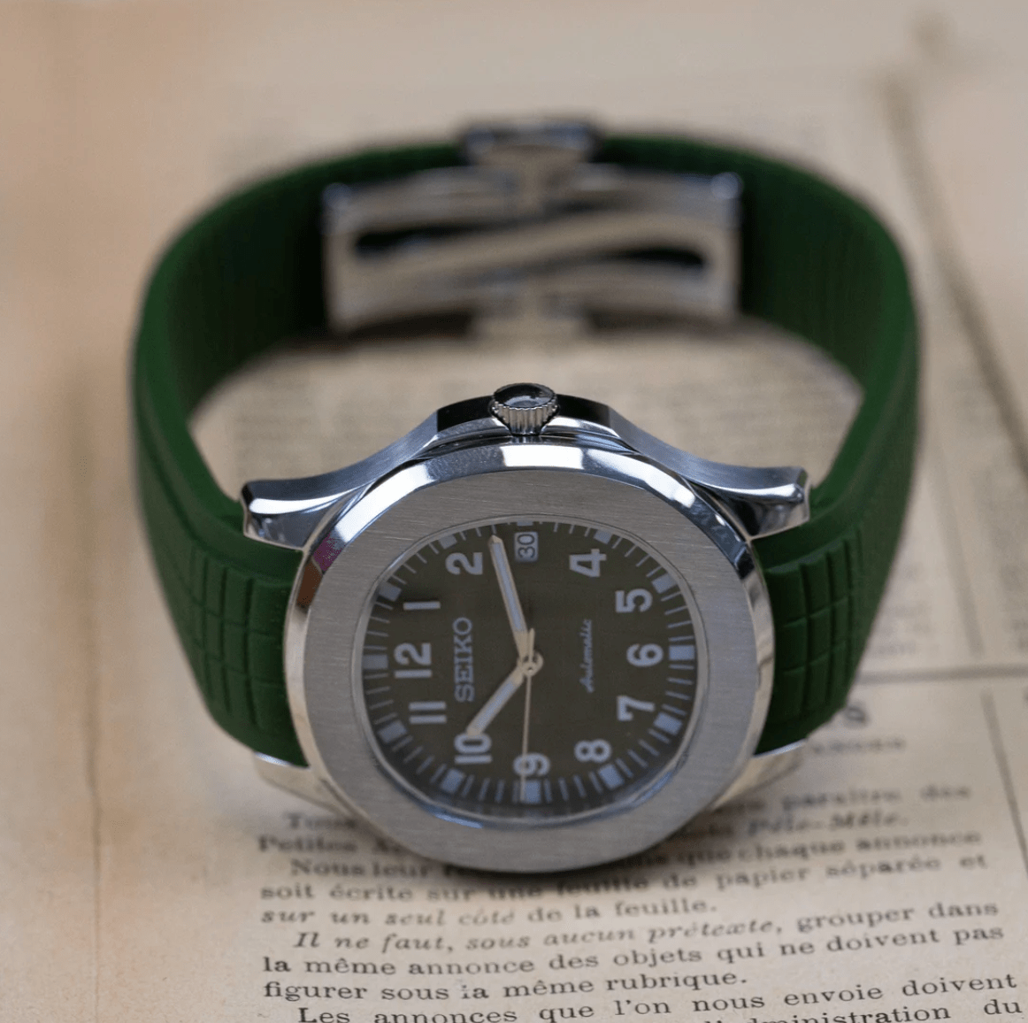 Montre automatique ModTime de style Aquanaut — configuration verte (NH35), bracelet vert, couronne au-dessus du cadran, sur le côté sur un journal