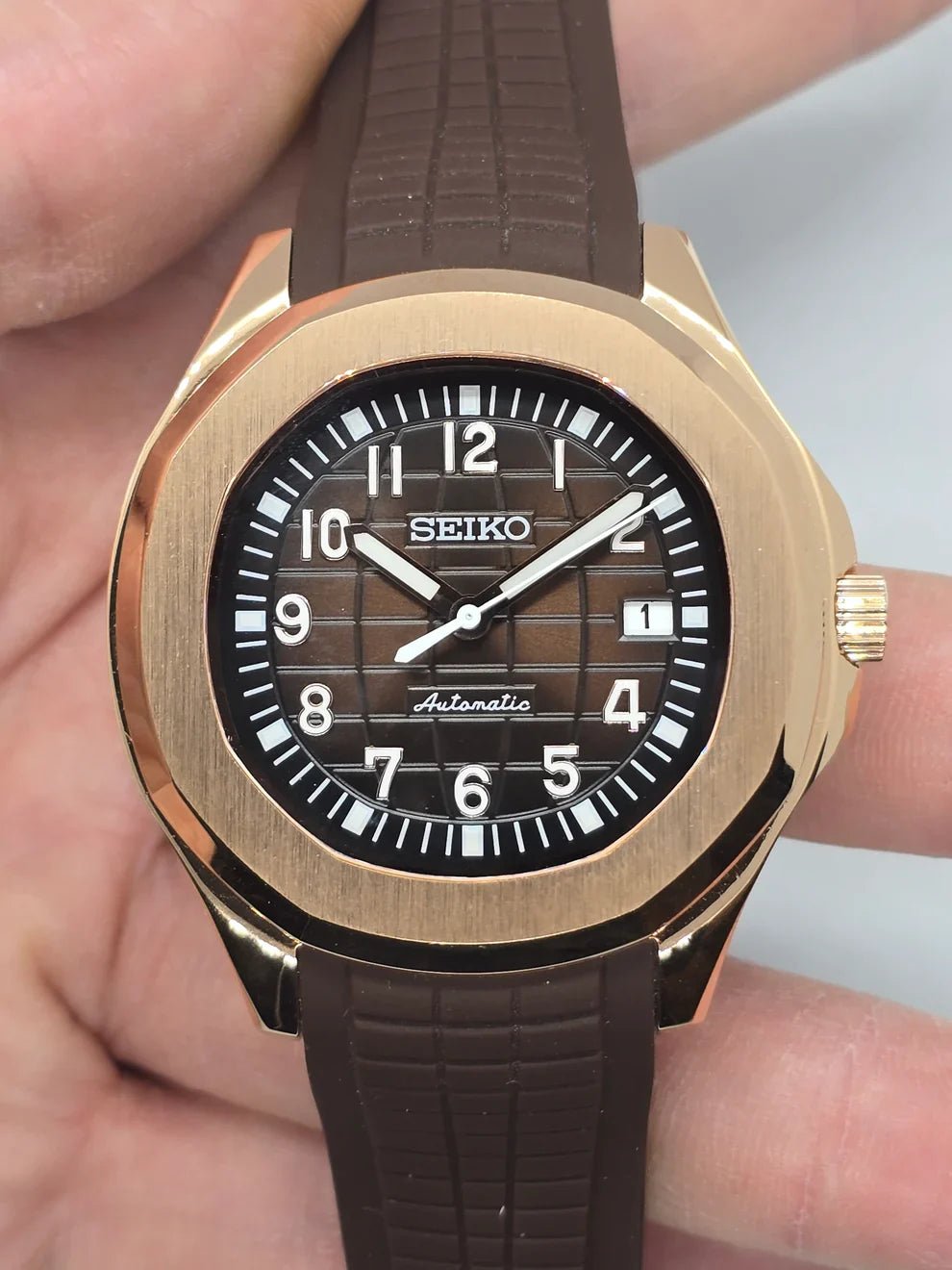 Montre automatique de style Aquanaut — configuration aux tons or rose, cadran marron (NH35) avec lunette aux tons or rose et date, vue de face tenue en main