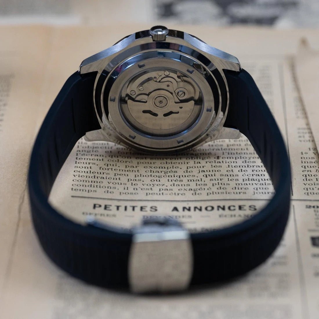 Montre automatique ModTime de style Aquanaut — configuration «Silver Back» (NH35), bracelet noir, fond de boîtier transparent, vue arrière sur un journal