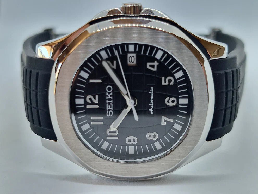 Montre automatique de style Aquanaut — configuration argentée, cadran noir (NH35) avec bracelet noir et guichet de date, posée sur le côté