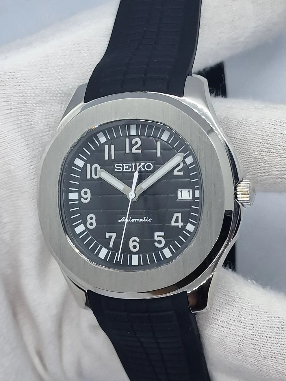 Montre automatique de style Aquanaut — configuration argentée, cadran noir (NH35) avec bracelet noir et couronne striée, en biais dans un gant
