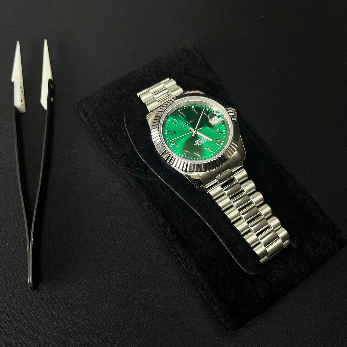 Montre automatique ModTime de style Datejust — configuration verte, à chiffres arabes (NH35), bracelet aux tons argentés, maillons arrondis, posée à plat à côté d'une pince