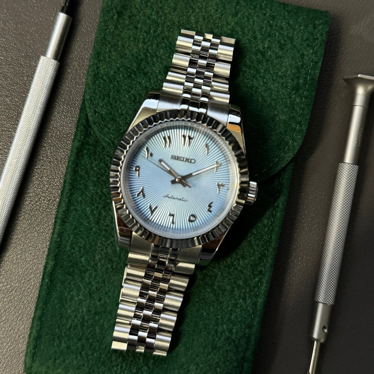 Montre automatique ModTime de style Datejust — configuration argentée et bleu clair, à chiffres arabes (NH35), bracelet aux tons argentés, lignes radiales, sur un coussin vert