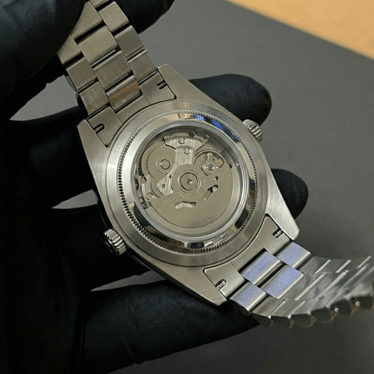 Montre automatique de style Datejust — configuration cadran vert olive à chiffres arabes (NH35) avec rotor aux tons argentés, gros plan arrière dans un gant