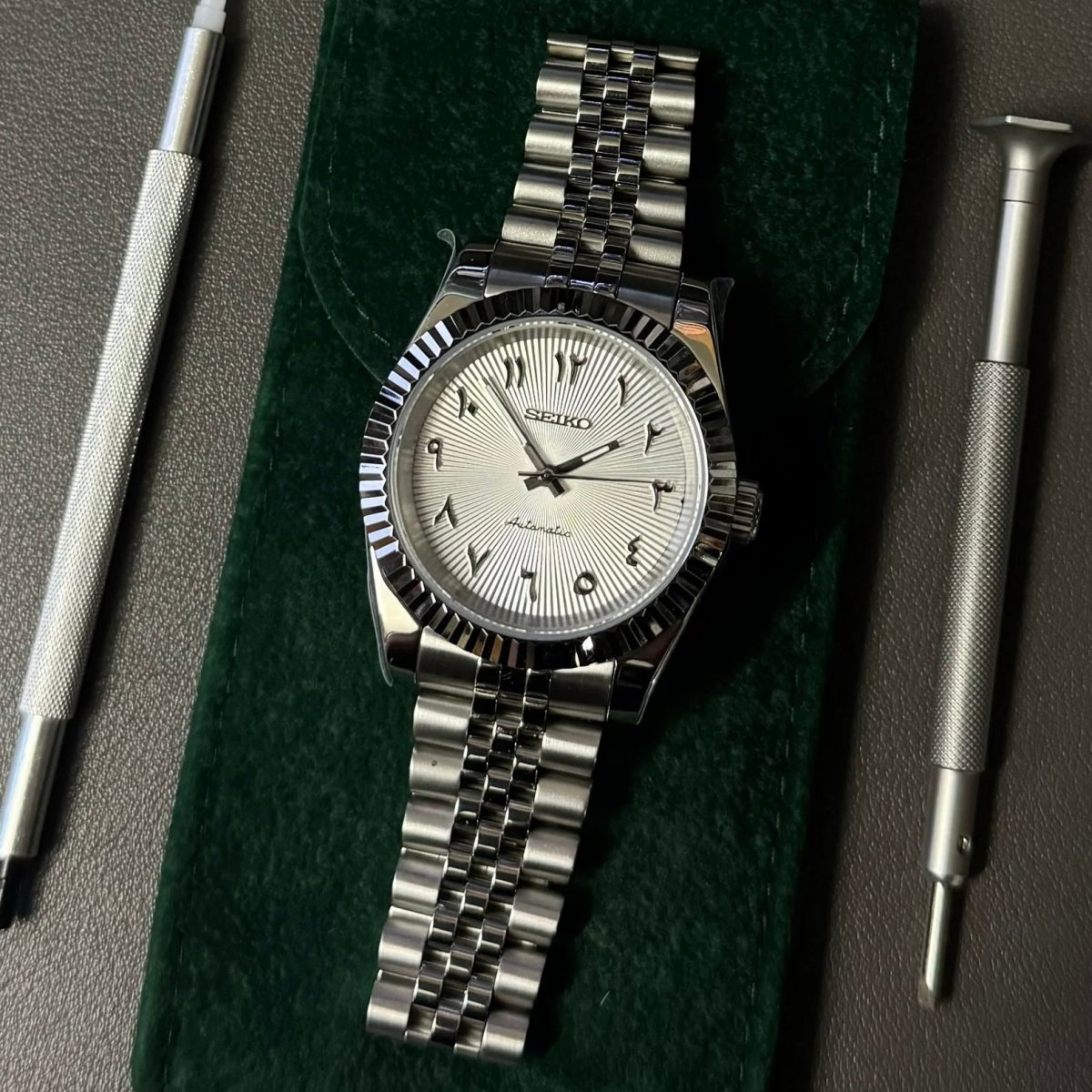 Montre automatique ModTime de style Datejust — configuration blanche, à chiffres arabes (NH35), bracelet aux tons argentés, maillons polis, posée à plat sur fond vert
