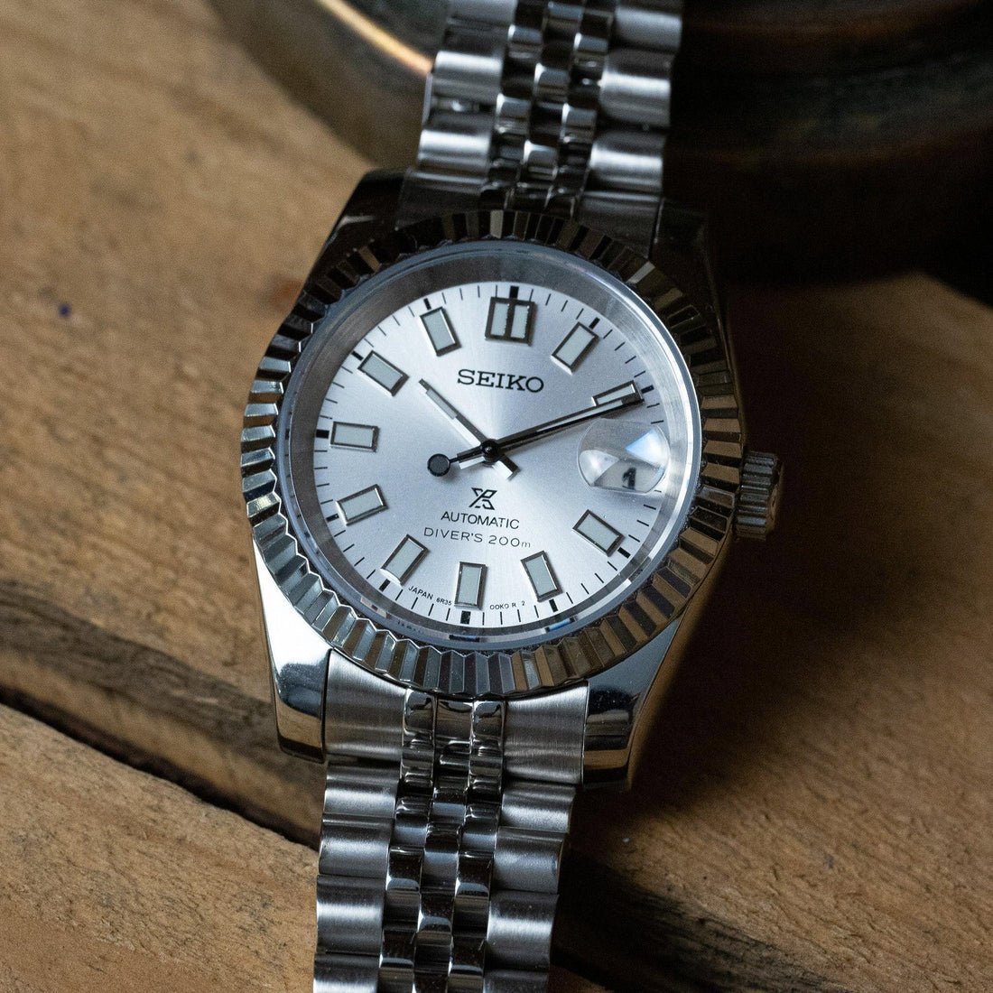 Fiche du modèle ModTime de style Datejust — configuration argentée et blanche (NH35) : cadran blanc portant l'inscription 6R35, gros plan sur un coussin beige