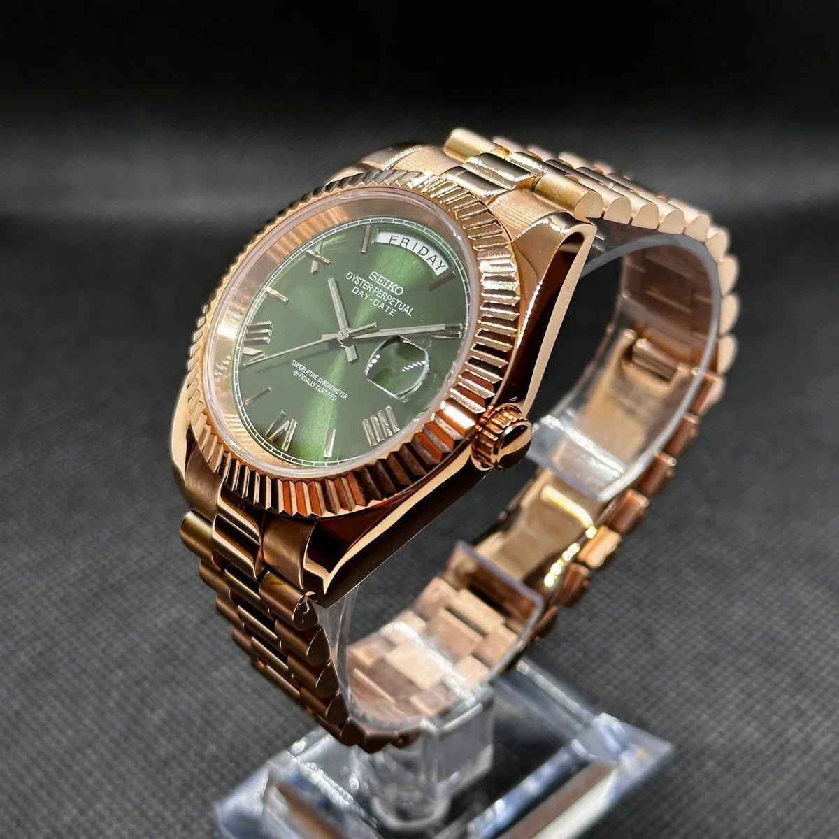 Montre ModTime de style Daydate — configuration aux tons or rose et olive (Miyota 8285), cadran olive, lunette cannelée et couronne, vue en biais sur un support