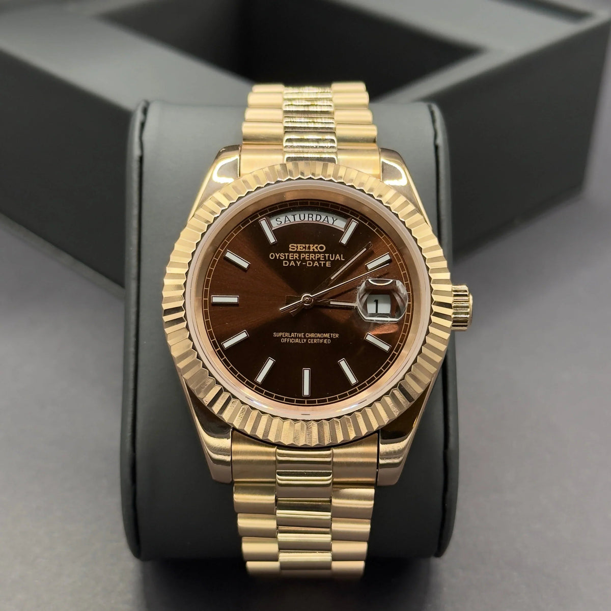 Montre ModTime de style Daydate — configuration chocolat (Miyota 8285), cadran marron soleillé, index horaires bâtons, gros plan sur un coussin