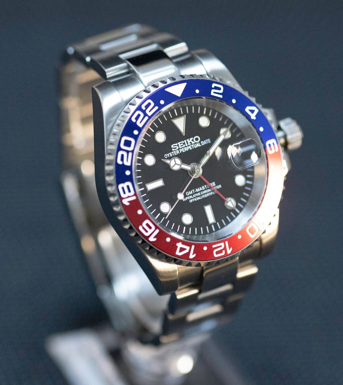 Montre automatique GMT — configuration «Pepsi» (NH34) avec boîtier aux tons argentés et aiguille GMT rouge, vue de trois quarts côté gauche