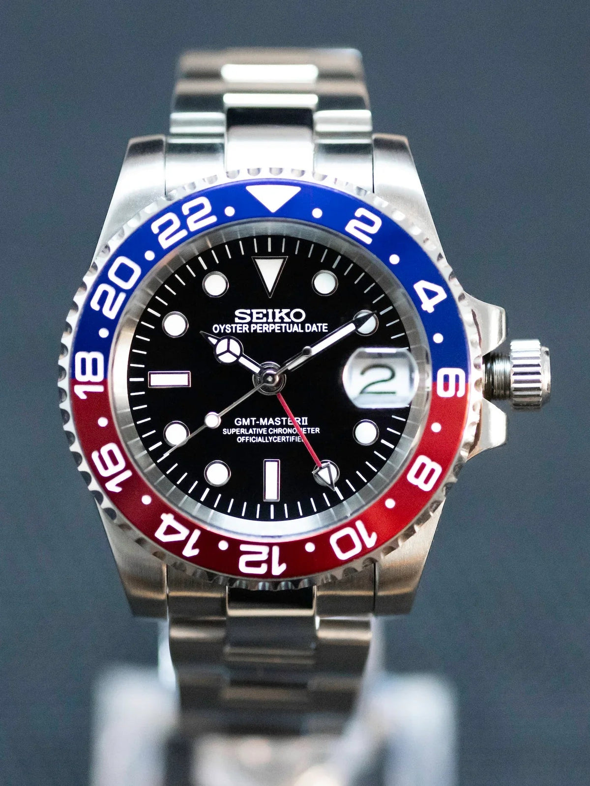 Montre automatique GMT — configuration «Pepsi» (NH34), gros plan frontal du cadran noir, aiguille GMT rouge et date agrandie