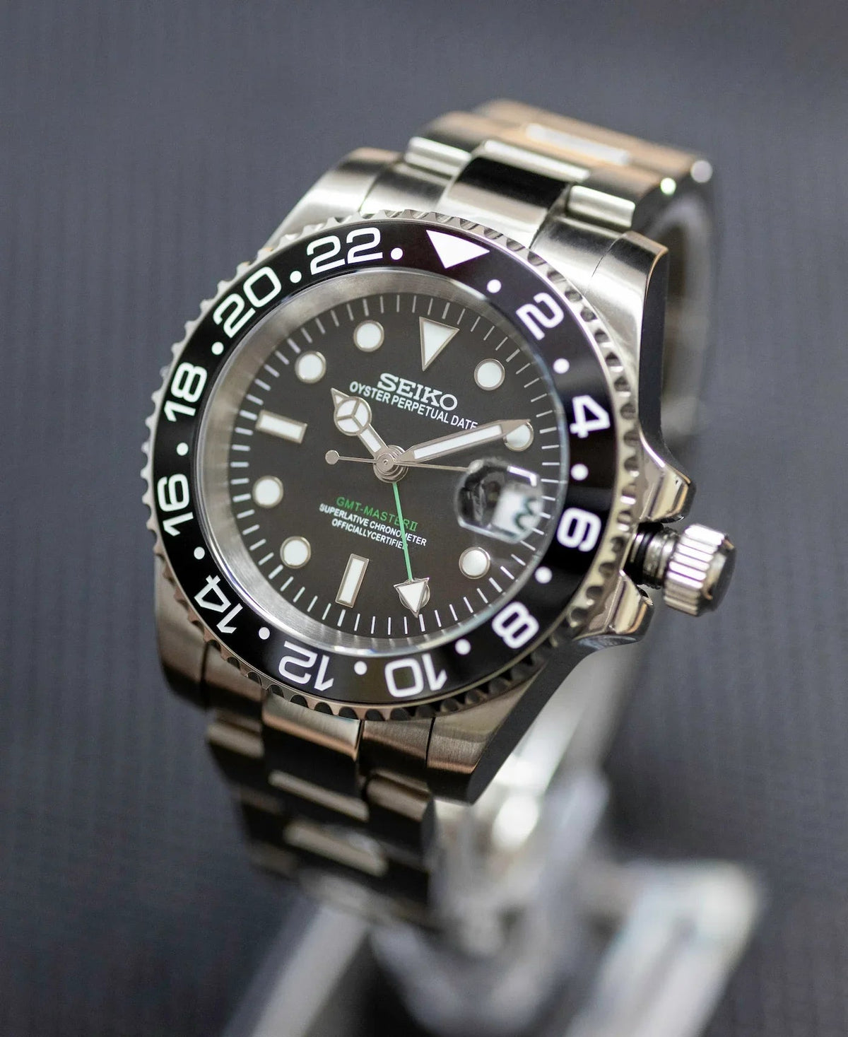 Montre automatique GMT — configuration noire (NH34) avec cadran noir et couronne sortie, vue en biais côté couronne
