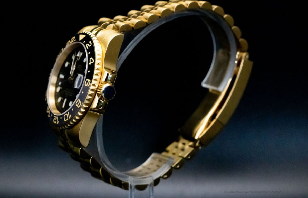 Montre automatique GMT — configuration aux tons dorés et noirs (NH34) avec boîtier aux tons dorés et couronne striée, profil côté couronne sur un support