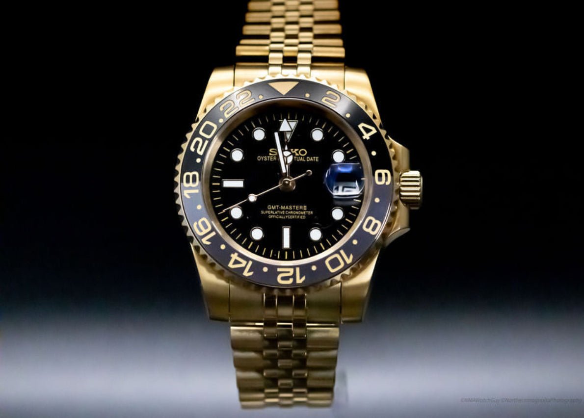 Montre automatique GMT — configuration aux tons dorés et noirs (NH34) avec lunette noire et chiffres aux tons dorés, vue de face sur fond sombre