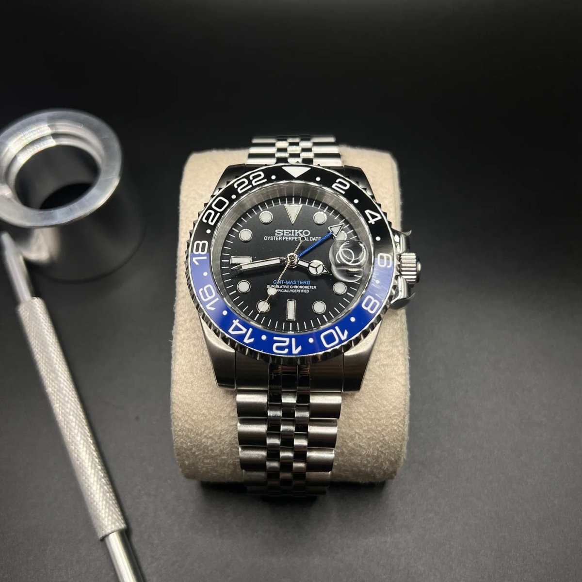 Montre automatique GMT — configuration «Batgirl» (NH34) avec une lunette bleue et noire et un bracelet de style Jubilee sur un coussin à côté d'outils