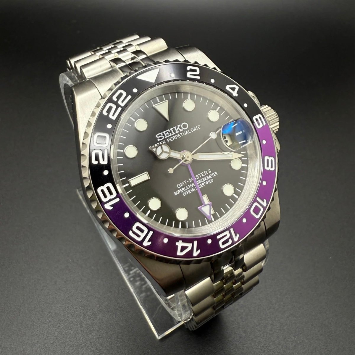 Montre automatique GMT — configuration «Joker» (NH34) avec cadran noir et loupe de date surélevée, vue en biais du côté gauche