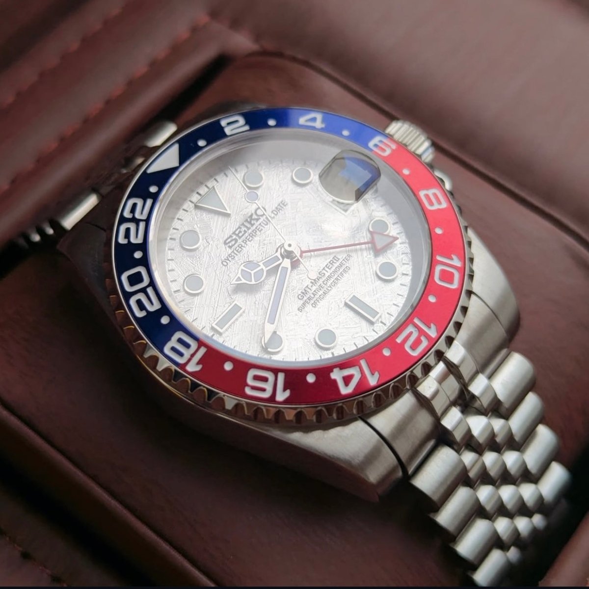 Montre automatique GMT — configuration «Meteorite» (NH34) avec cadran argenté et maillons de style Jubilee, vue depuis un angle bas du côté gauche