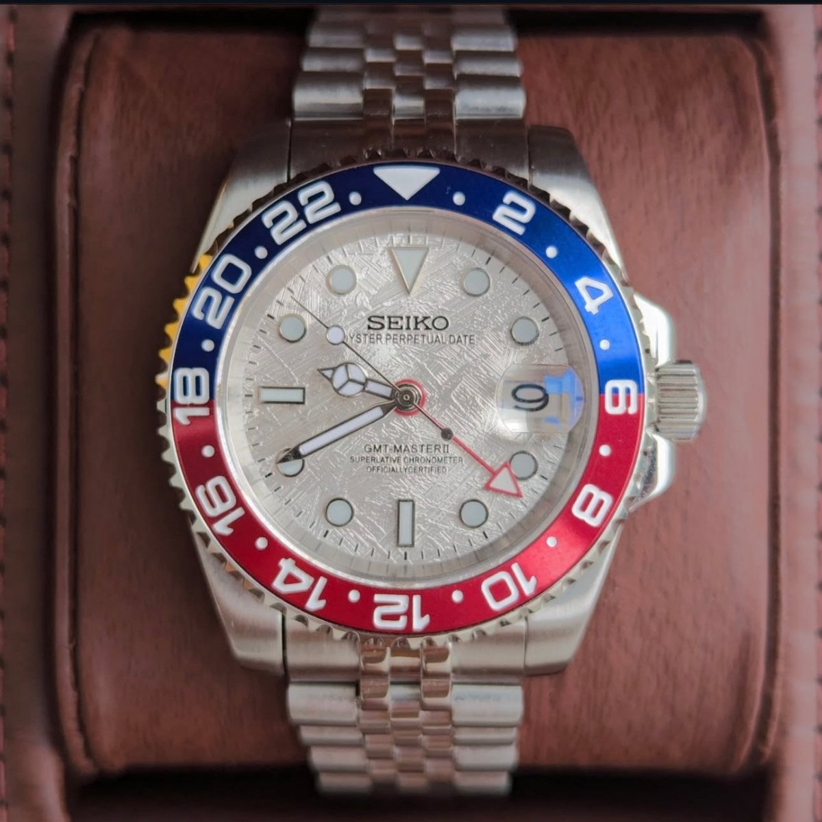 Montre automatique GMT — configuration «Meteorite» (NH34) avec cadran argenté à motif et aiguille GMT rouge, gros plan frontal