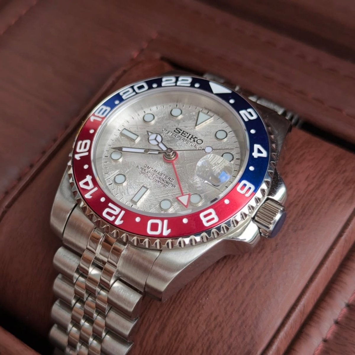 Montre automatique GMT — configuration «Meteorite» (NH34) avec lunette rouge et bleue et couronne striée, vue depuis un angle bas côté couronne