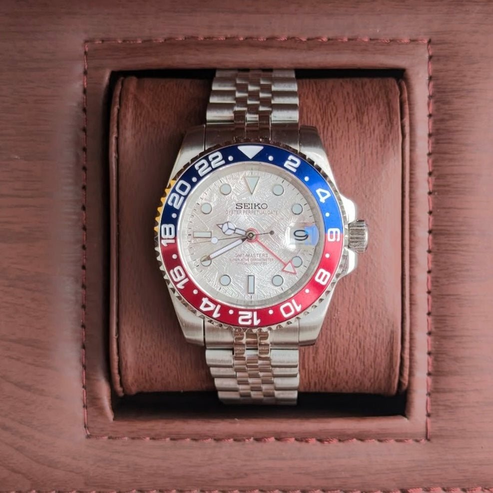 Montre automatique GMT — configuration «Meteorite» (NH34) avec cadran argenté et bracelet de style Jubilee, vue du dessus dans une boîte marron