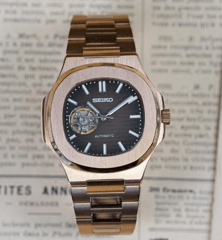 Montre automatique de style Nautilus — configuration chocolat, cœur ouvert (NH38) avec cadran marron et index bâtons, sur un journal