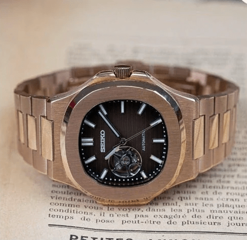 Montre automatique de style Nautilus — configuration chocolat, cœur ouvert (NH38) avec maillons aux tons or rose, sur le côté sur du papier