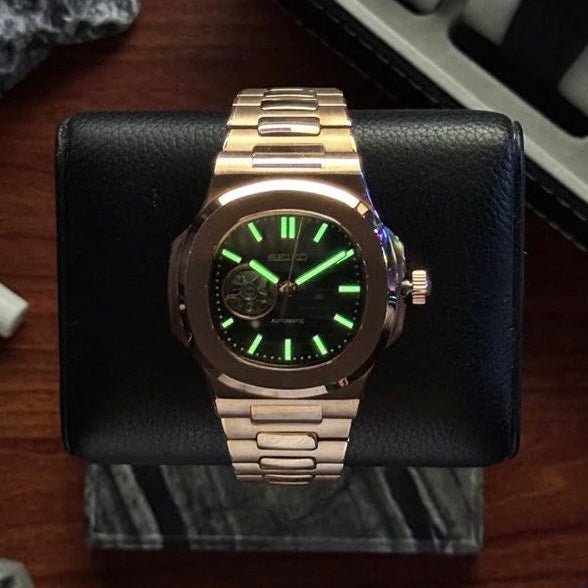 Montre automatique ModTime de style Nautilus — configuration aux tons or rose et noirs, cœur ouvert (NH38), cadran noir, aiguilles lumineuses vertes, vue sous une faible lumière
