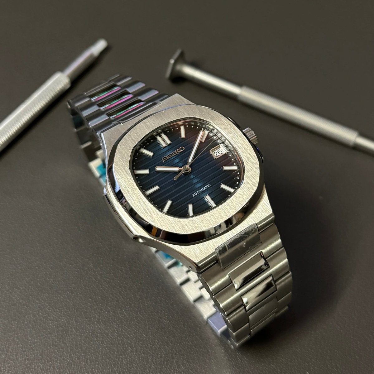Montre automatique de style Nautilus — configuration argentée, cadran bleu (NH35) avec cadran bleu, index bâtons, à côté d'outils