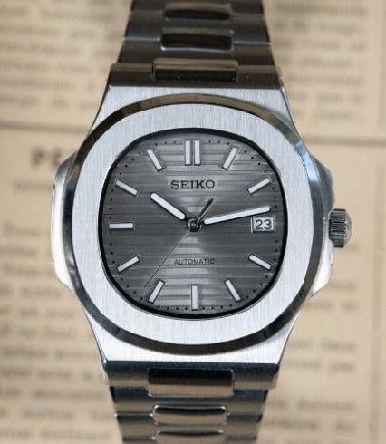 Montre automatique de style Nautilus — configuration cadran argenté (NH35) avec maillons aux tons argentés, index bâtons, vue de face sur un journal