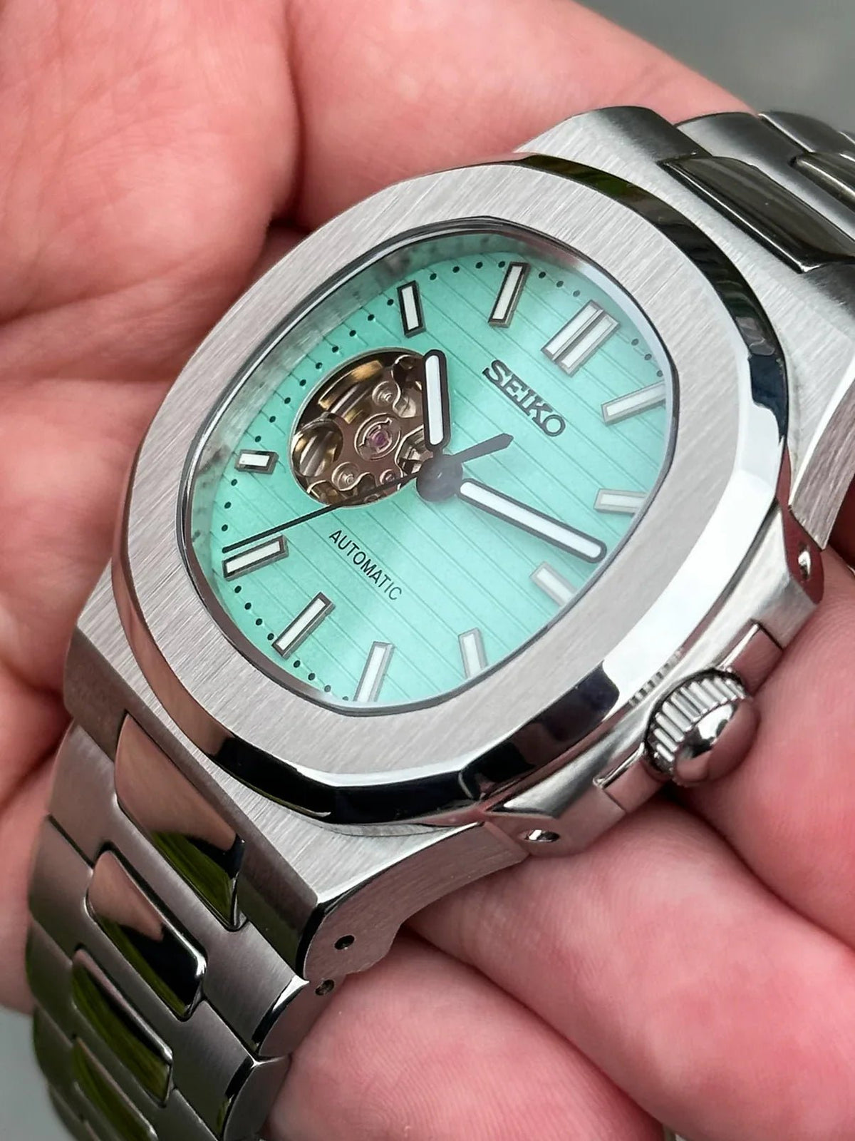 Montre automatique ModTime de style Nautilus — configuration «Tiffany», cœur ouvert (NH38), boîtier aux tons argentés, couronne striée, vue en biais tenue en main
