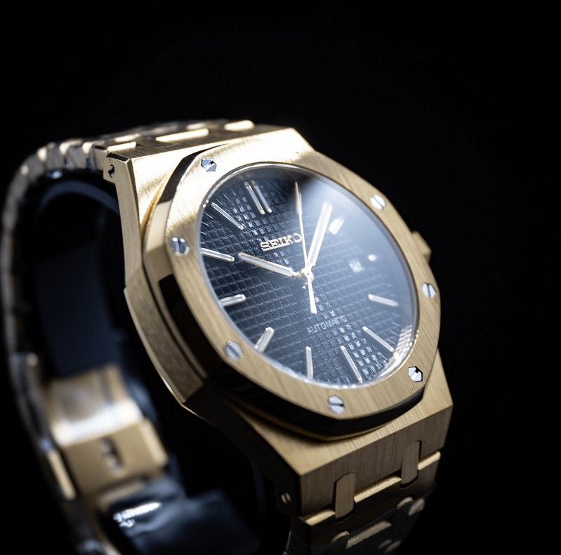 Montre automatique de style Royal Oak — configuration cadran noir (NH35) avec maillons aux tons dorés, cadran quadrillé, vue depuis un angle bas à gauche