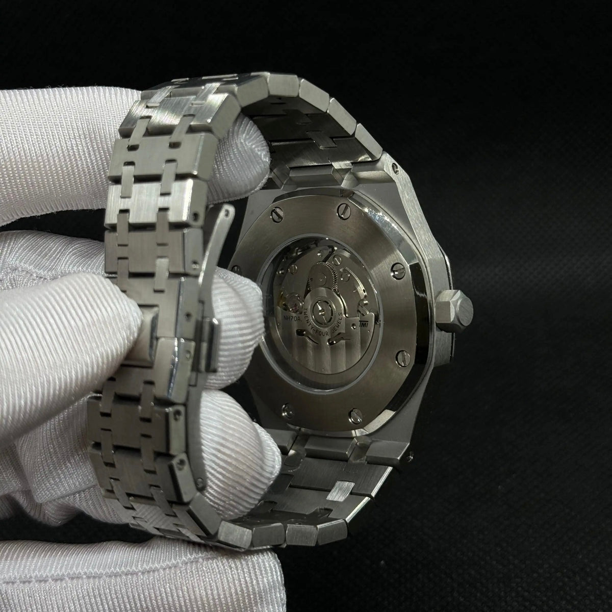 Fiche du modèle ModTime de style Royal Oak — configuration argentée, squelette (NH38) : fond du boîtier aux tons argentés, rotor portant l'inscription NH70A, vue arrière tenue dans une main gantée