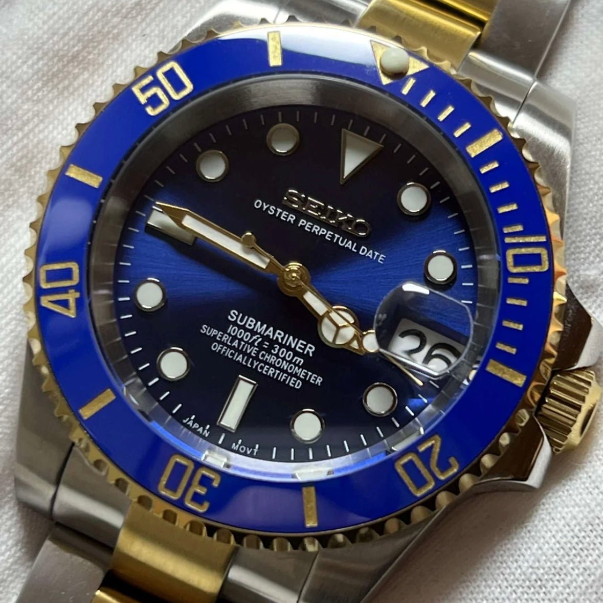 Montre automatique de style Submariner — configuration bicolore, «Ocean» (NH35) avec cadran bleu, finition soleillée, gros plan tenu dans une main gantée