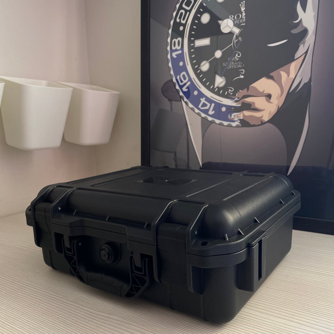 Boîte Watch Security Box noire ModTime, couvercle fermé, deux fermoirs avant et poignée de transport, vue en biais sur un bureau